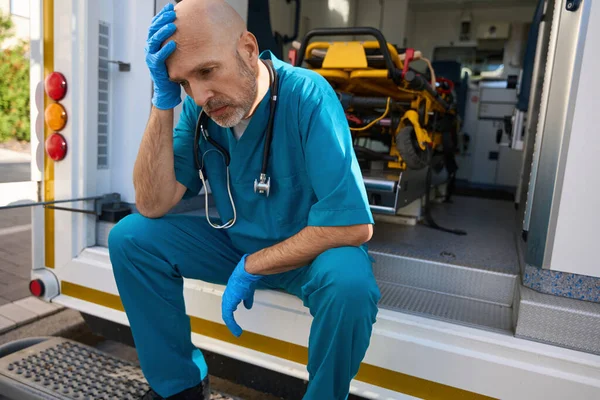 Überlasteter Mann Arztuniform Sitzt Rand Eines Krankenwagens Während Seine Hand — Stockfoto