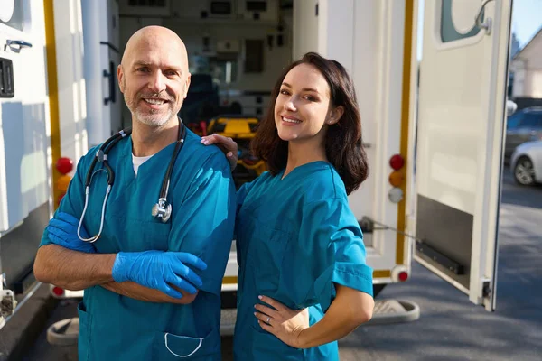 救急車のチームの幸せな医者は半回転で滅菌手袋に立っている間彼のパートナーは彼女の手で彼の肩に触れる — ストック写真