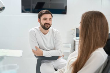 Gülümseyen genç erkek dişçi, ilk muayenede kadın hastayla iletişim kuruyor.