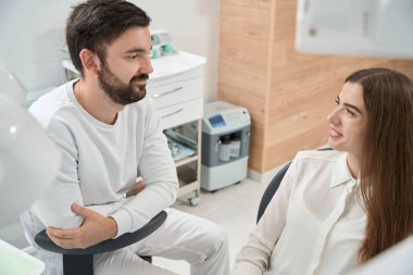 Gülümseyen diş hekimi muayenesi sırasında doktorla konuşuyor.