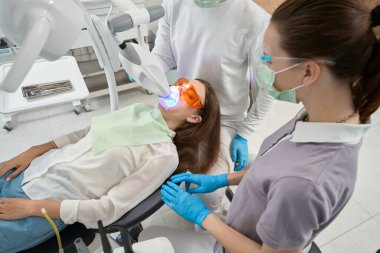 Nitelikli doktor hasta diş minesinin üzerinde LED açık diş beyazlatma lambası kullanıyor.