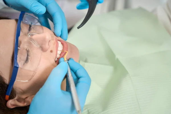 Patient in safety goggles lying supine while dental hygienist removing tartar in her interdental spaces