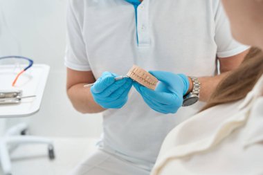 Azot eldivenli doktorun kesilmiş fotoğrafı hastaya diş modelini gösteriyor.