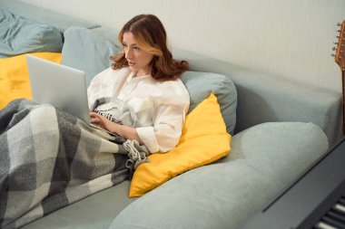 Taşınabilir bilgisayarda yazarken yatakta oturan sakin, odaklı genç bir kadın.