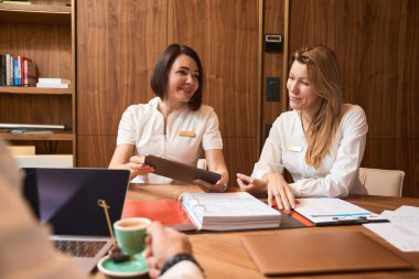 Kadın doktorlar elinde dizüstü bilgisayarla bir masada oturuyorlar. Bir meslektaşlarının karşısında çay içiyorlar.