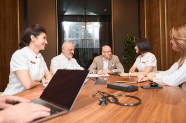 Başhekimin ofisindeki tedavi planının tartışılmasında personel büyük bir tahta masaya oturdu.