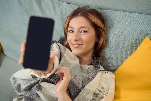 Smiling Pleased Young Woman Lying Bed Holding Smartphone Outstretched Hand —  Fotos de Stock
