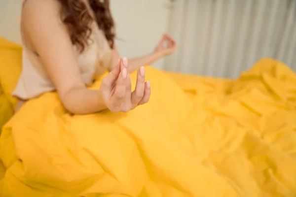 Cropped photo of woman seated in bed performing Shuni mudra using thumb and middle fingers