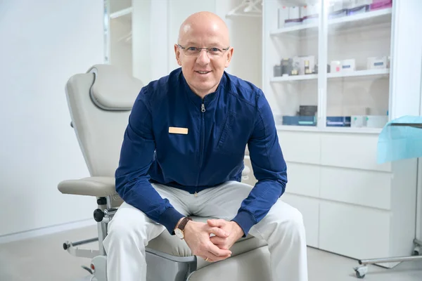 Joyful Clinic Employee Badge His Shirt Sits Medical Chair Background — Stockfoto