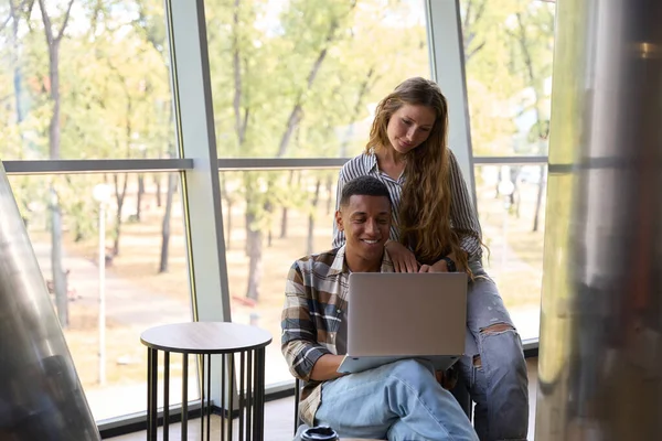Man and woman looking at laptop screen against large window, copy space