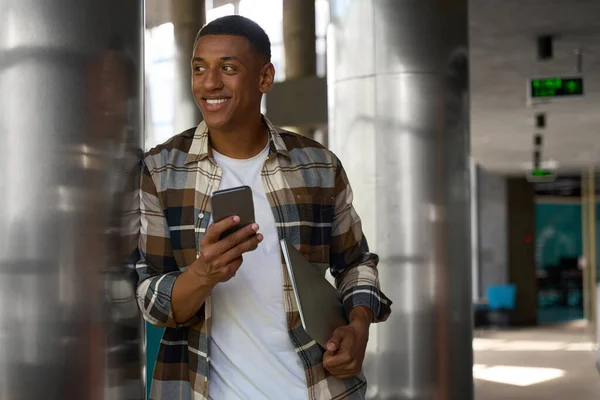 Glad Afroamerikansk Man Som Använder Smartphone Medan Håller Laptop Kontoret — Stockfoto