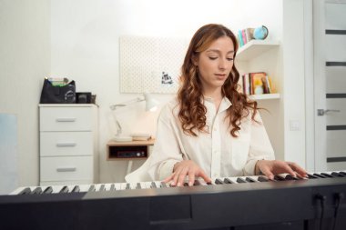 Waist-up portrait of serious young female musician performing musical composition on synthesizer