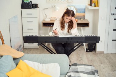 Serious concentrated musician seated at synthesizer with pencil in hand staring at sheet music