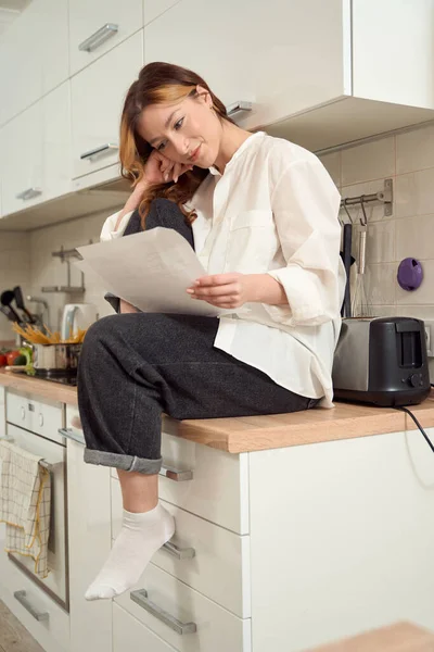 Focused Lady Seated Kitchen Counter Looking Documents Her Hands — Stock fotografie