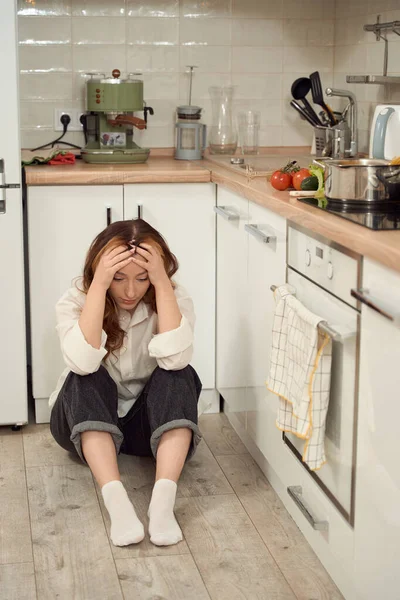 キッチンで一人で床に座って下を見下ろす絶望的な女性 — ストック写真