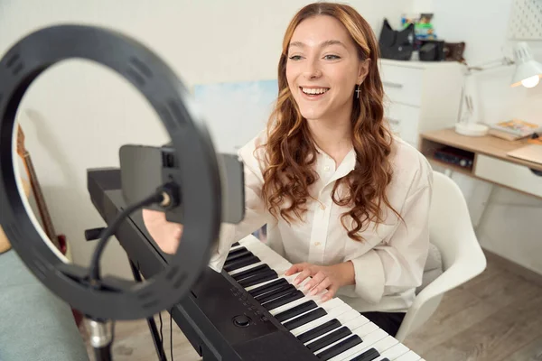 Smiling Pleased Young Keyboardist Sitting Synthesizer Adjusting Settings Cellphone — Foto Stock