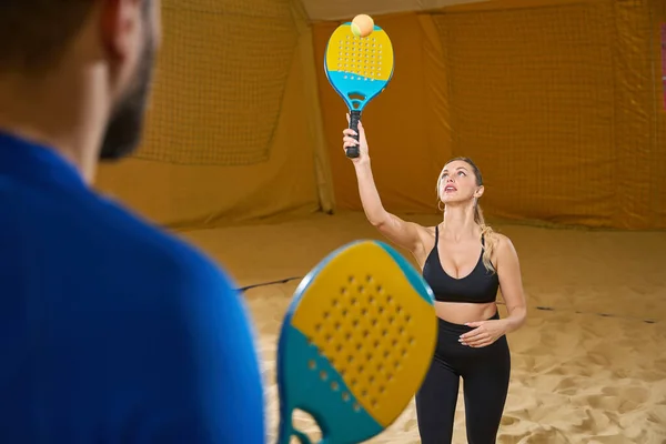 Attentive Female Sportswear Playing Beach Tennis Indoors While Man Stands — Zdjęcie stockowe