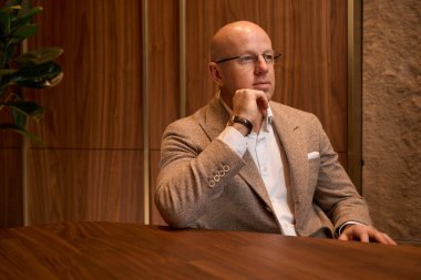 Iimposing man in beige jacket sits in a room with a stylish eco-design with a living panel and wooden walls