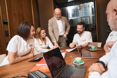 Head of medical clinic actively communicates with colleagues at a working meeting, the team is seated at a large table