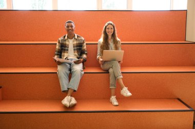 Two smiling students sitting on steps and using gadgets in university