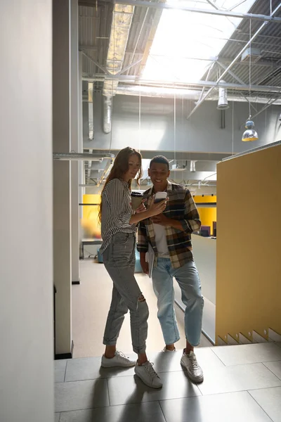Full-length photo of man and woman looking at phone screen while standing in the office hall
