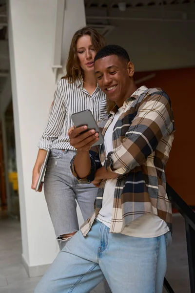 Smiling African American guy and young lady looking at smartphone screen indoors
