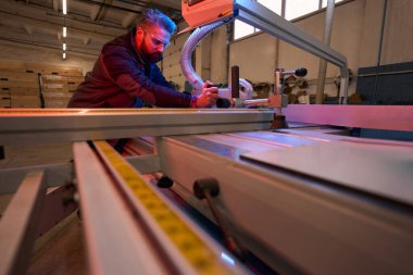 Worker in protective clothes standing near form cutting machine and repairing it in workshop