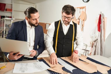 Serious fashion designers standing at cutting table and arranging pattern pieces on fabric