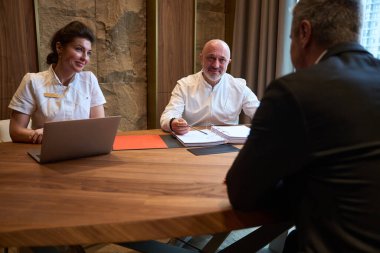 Friendly doctors and a client in a stylish suit are sitting at a desk discussing a treatment plan