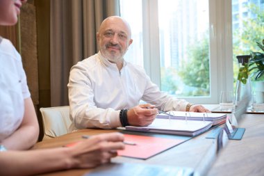 Ggray-haired man and young woman are sitting at work desk in a medical clinic, working papers are on the table
