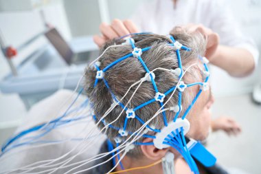 Middle-aged man undergoes a check-up in a modern clinic, the doctor conducts a diagnostic procedure for him EEG - electroencephalography
