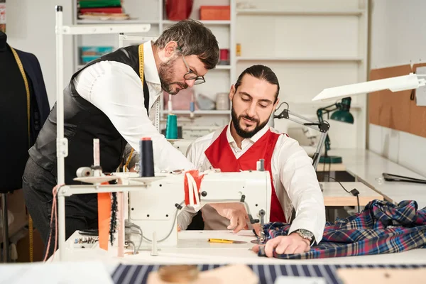 Serious Focused Young Man Overcasting Fabric Serger Guidance Experienced Tailor — Stok fotoğraf