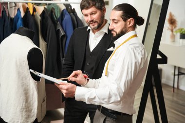 Serious fashion designer pointing with pencil at sheet of paper with rough drawing to his customer
