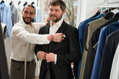 Smiling happy clothier checking fit of new suit on his pleased customer