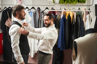 Smiling pleased tailor measuring chest width of adult man in his workshop