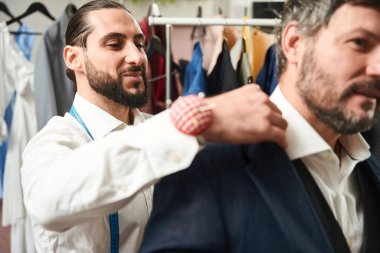 Smiling happy professional tailor trying on new item of clothing on adult man
