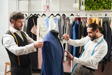 Focused tailor marking item of clothing with chalk pencil assisted by colleague