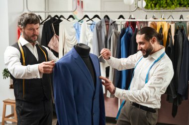 Smiling fashion designer marking client jacket with chalk pencil assisted by his colleague clipart