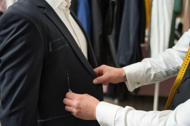 Cropped photo of clothier drawing vertical line with piece of chalk on customer garment
