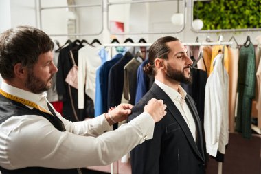 Serious focused clothier pinning jacket sleeve to armhole on calm male client