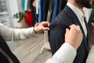 Cropped photo of tailor adjusting length of sleeve on client using pins