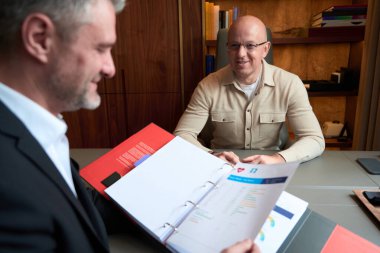 Waist up portrait of handsome European man is having conversation with business man while they discussing the documents in the office