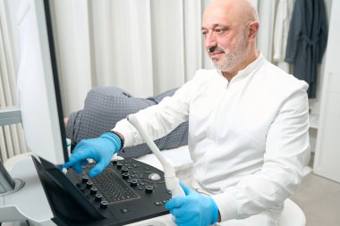 Close up portrait of handsome Caucasian man doctor is looking to the screen of modern medicine device for examining indicators of health