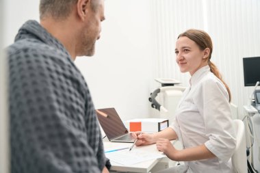 Side view portrait of smiling elegant female doctor is talking with patient in his medicine office