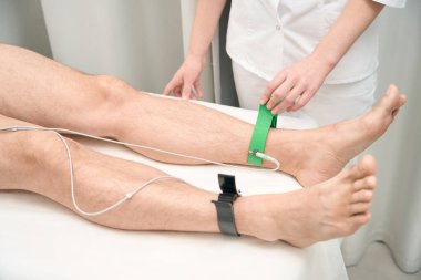 Close up portrait of process installing electrodes on patient legs for examining health indicators in modern hospital