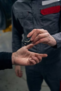 Mechanic in protective clothes standing in tire fitting, holding car keys and giving it to client