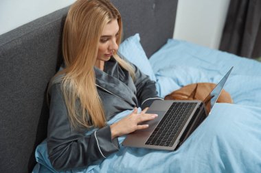 Tranquil focused woman working on portable computer in bed while her pet sleeping
