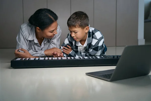 Loving african american mom teaches son to play digital piano, they have fun together