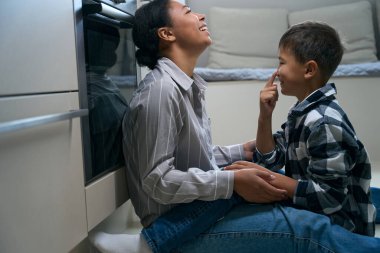 Joyful african american woman with son playing at home, boy on distance learning