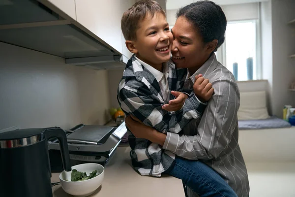 Happy Teenager Plaid Shirt Sits Kitchen Surface Mom Hugs Him — Fotografia de Stock